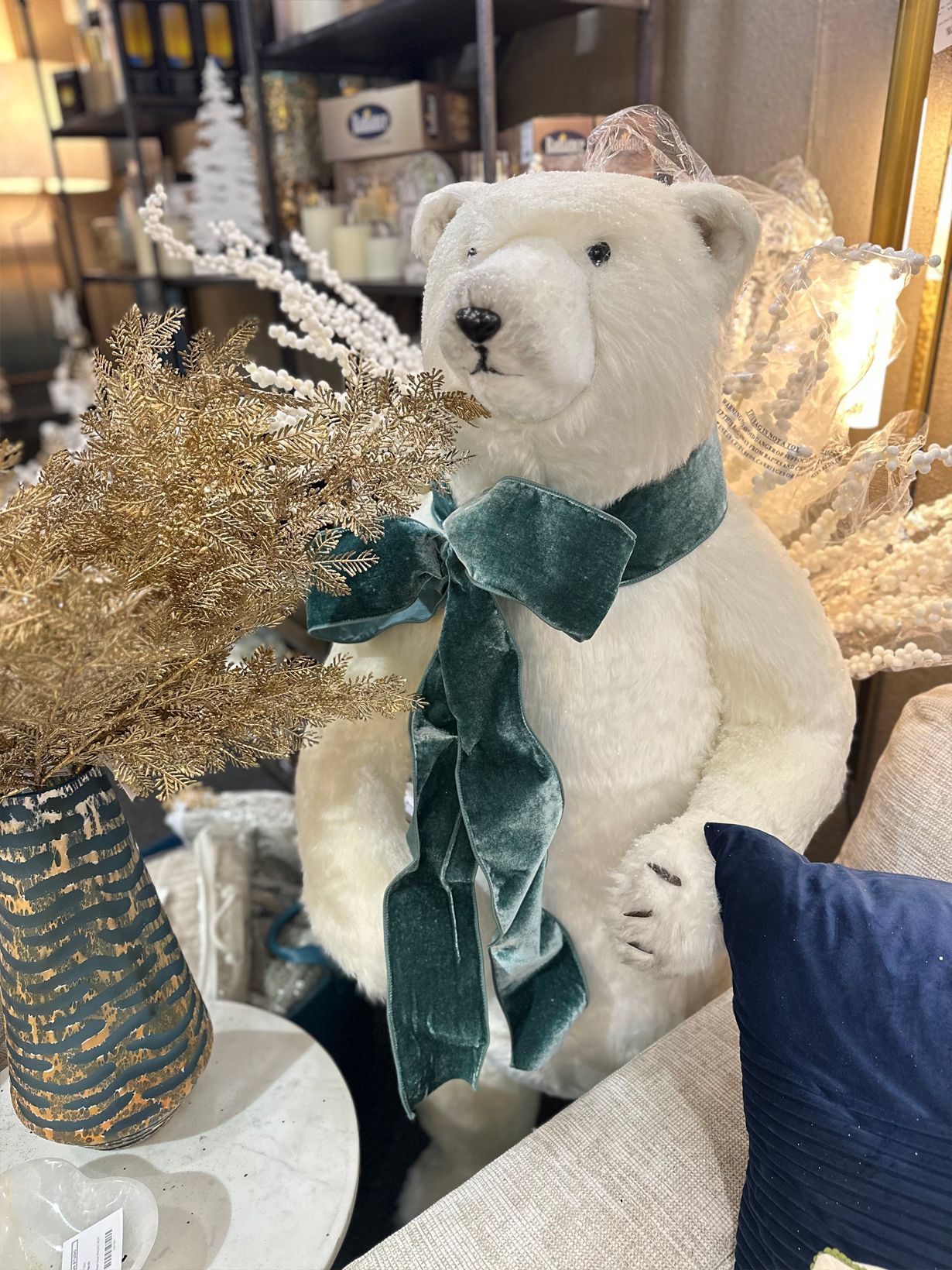 White teddy bear with teal ribbon among gold decor and pillows in a cozy home setting