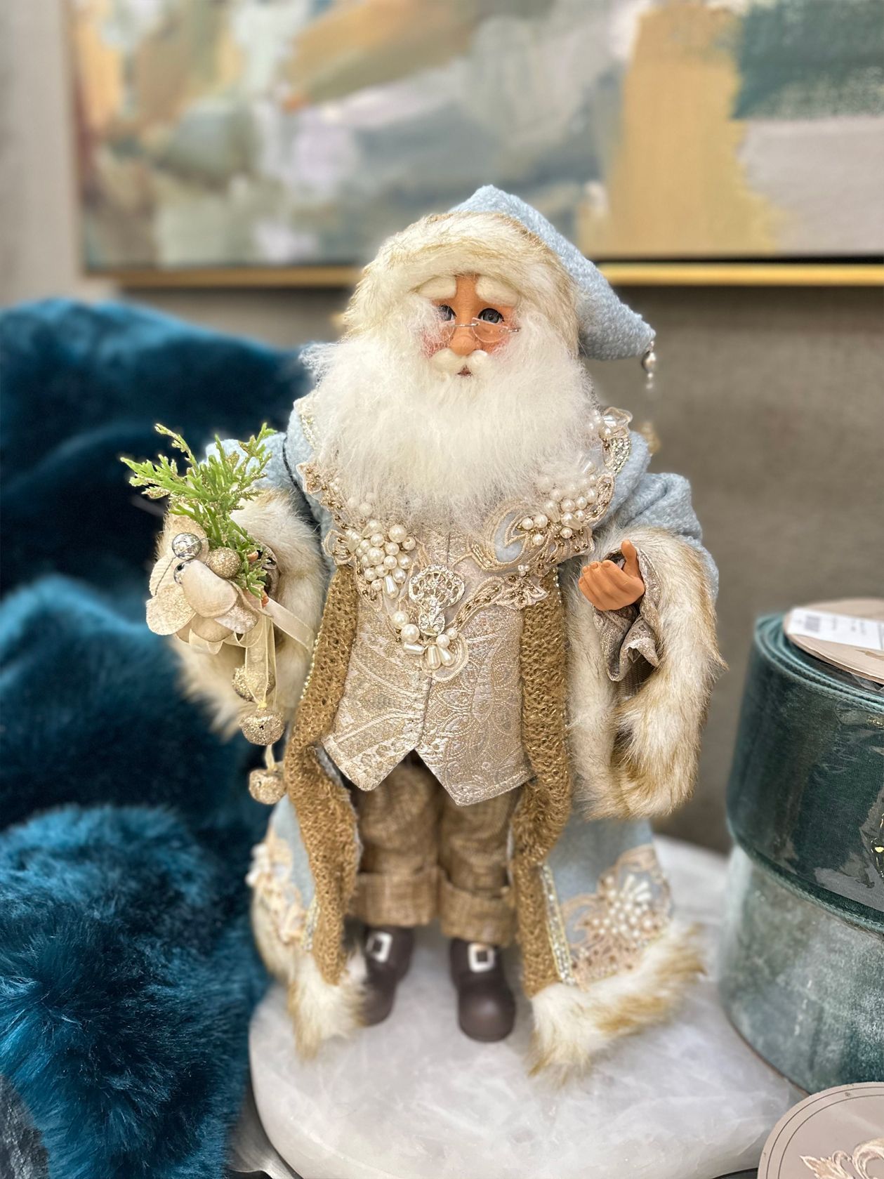 Santa figurine in a cream fur-trimmed coat and hat, holding white flowers on a table.