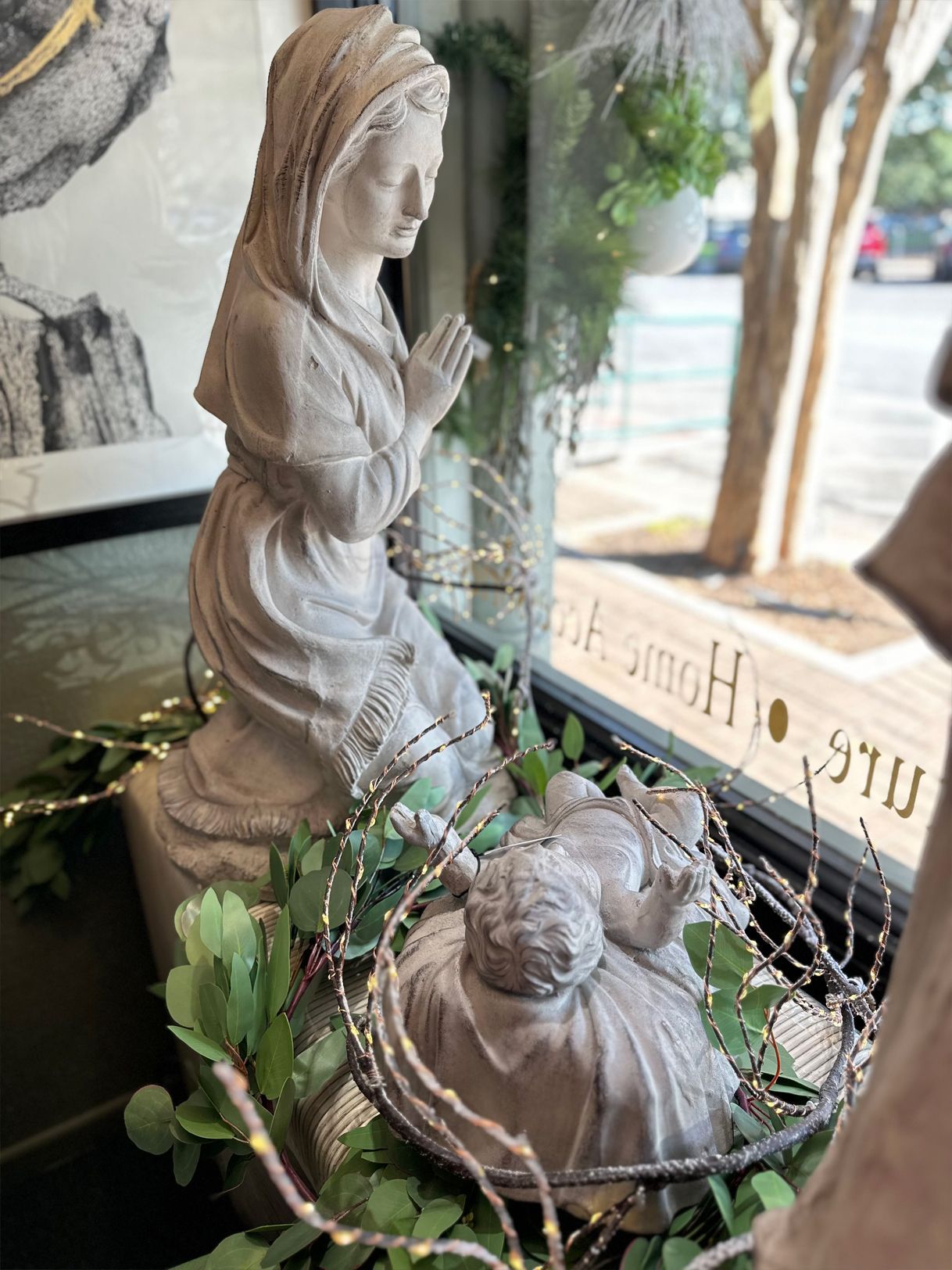 Stone Nativity scene with Mary, baby Jesus, and greenery in a window display