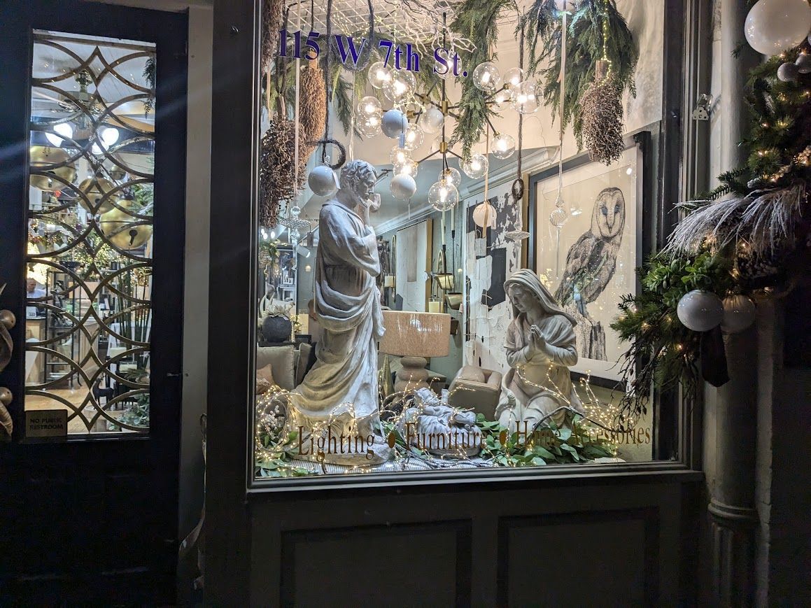 Festive shop window with white holiday figurines, greenery, and warm lights behind glass