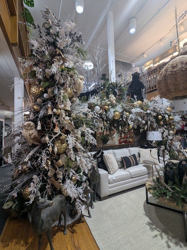 A festive showroom with a decorated Christmas tree, white sofa, and snow-dusted floral arrangements.