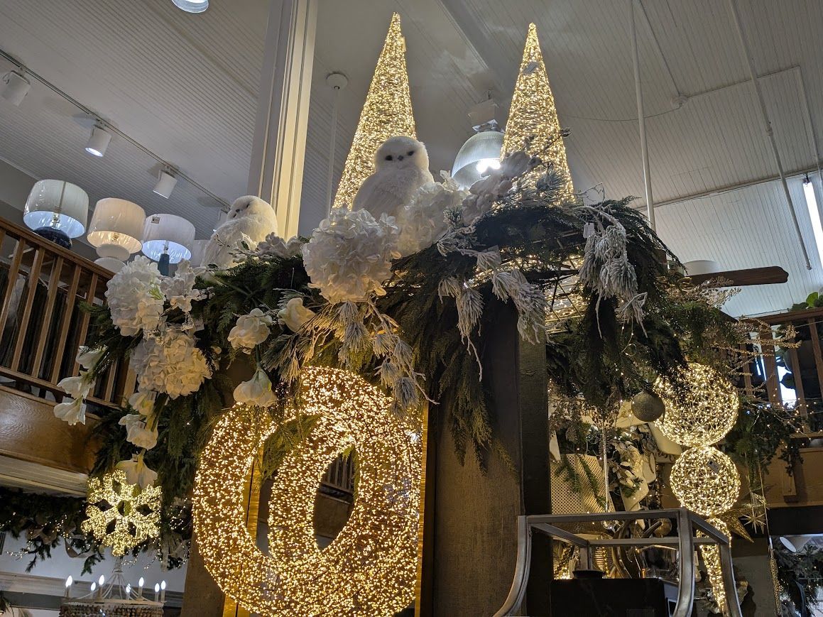 Decorated holiday display with lit reindeer, gold ornaments, and white flowers in a store window