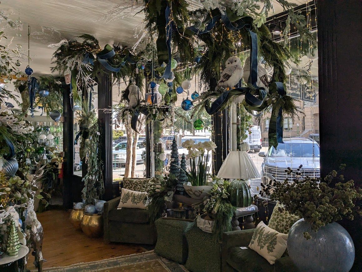 Decorated indoor space with hanging greenery, blue ornaments, and upholstered seating by large windows