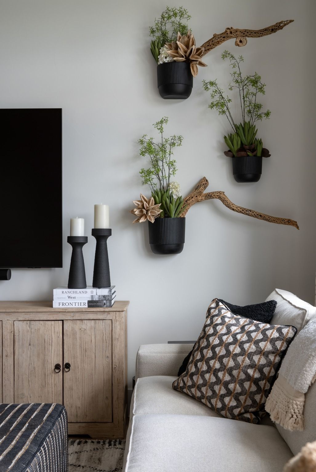Modern living room with wall-mounted black planters, a sofa with patterned pillows, and a wooden cabinet