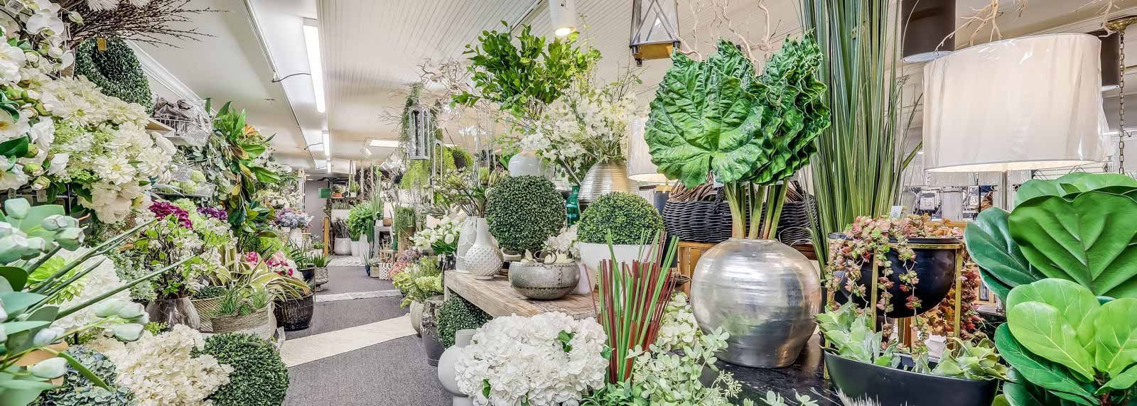 Lush indoor garden pathway with potted tropical plants, hanging greenery, and decorative moss balls