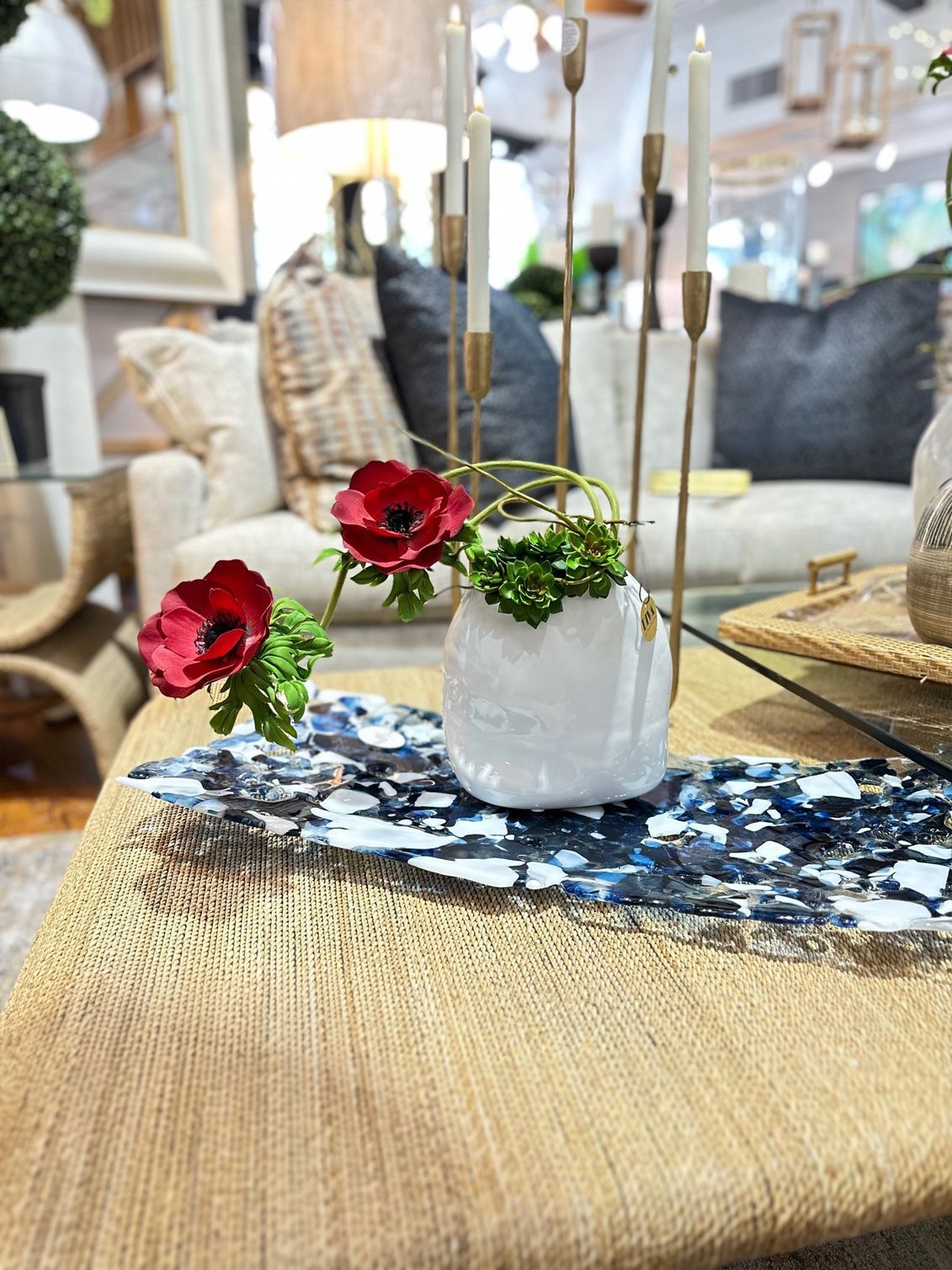 Small floral centerpiece in a white vase on a woven table runner in a bright living room.