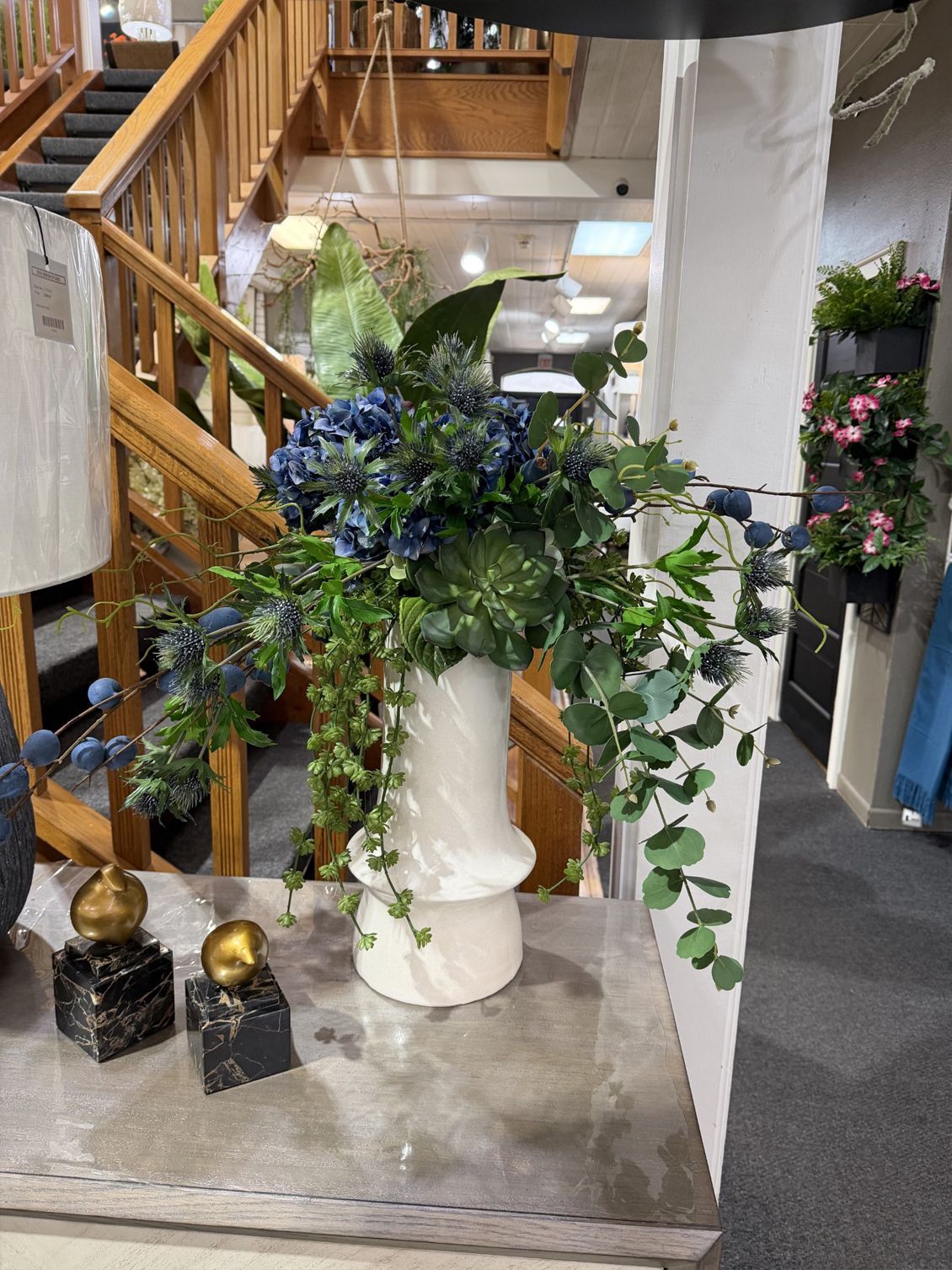 Decorative white pedestal planter with lush green and blue flowers in a showroom or store interior