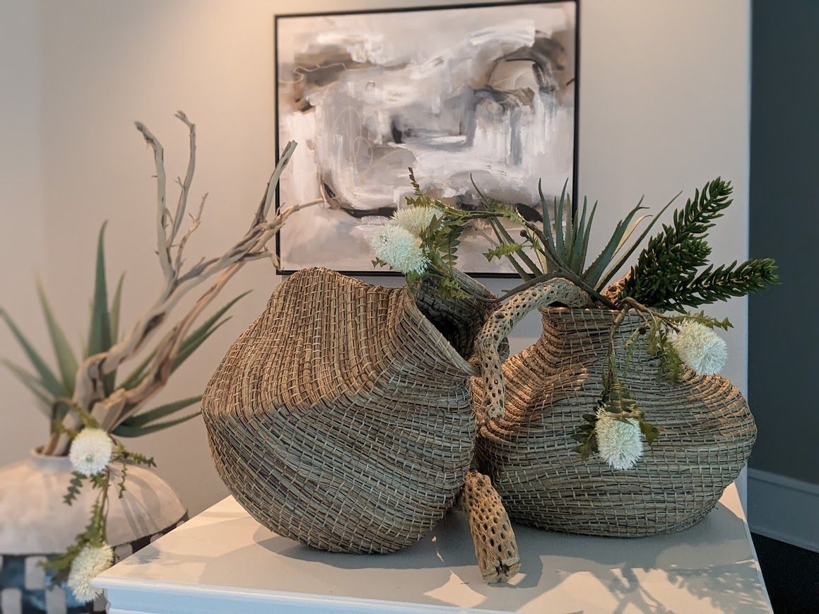 Decorative woven baskets with branches and flowers on a table beneath abstract wall art