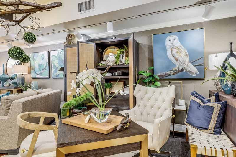 Cozy living room with tufted chairs, wood table, plants, owl artwork, and a decorative cabinet