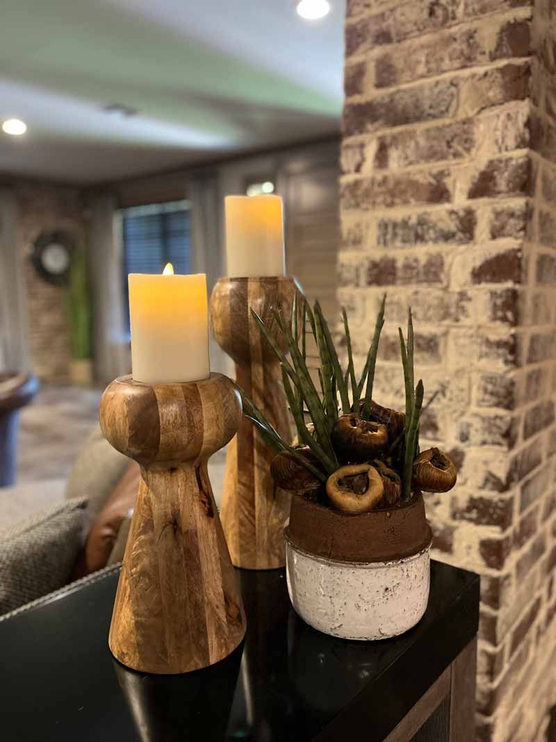 Decorative candles and a small plant arrangement on a table beside a brick wall