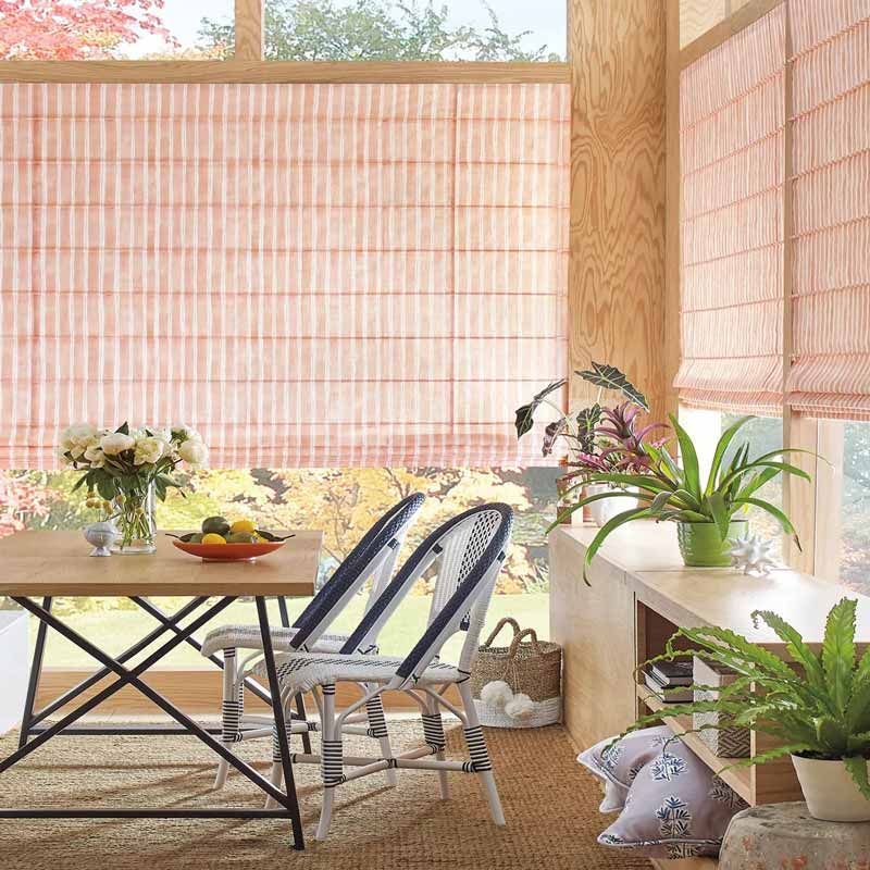 Bright patio with a wooden table, folded chairs, potted plants, and bamboo shades by the windows