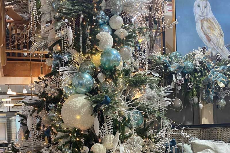 Decorated Christmas tree with silver, gold, and teal ornaments in a festive indoor lobby