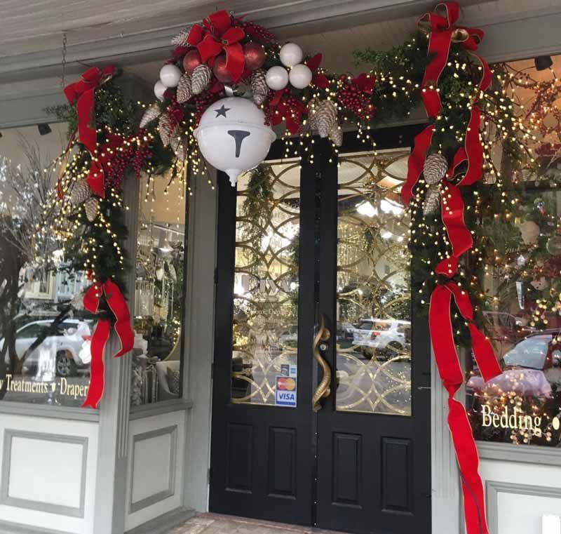 Festive storefront entrance with red ribbons, wreaths, and holiday lights around black double doors.