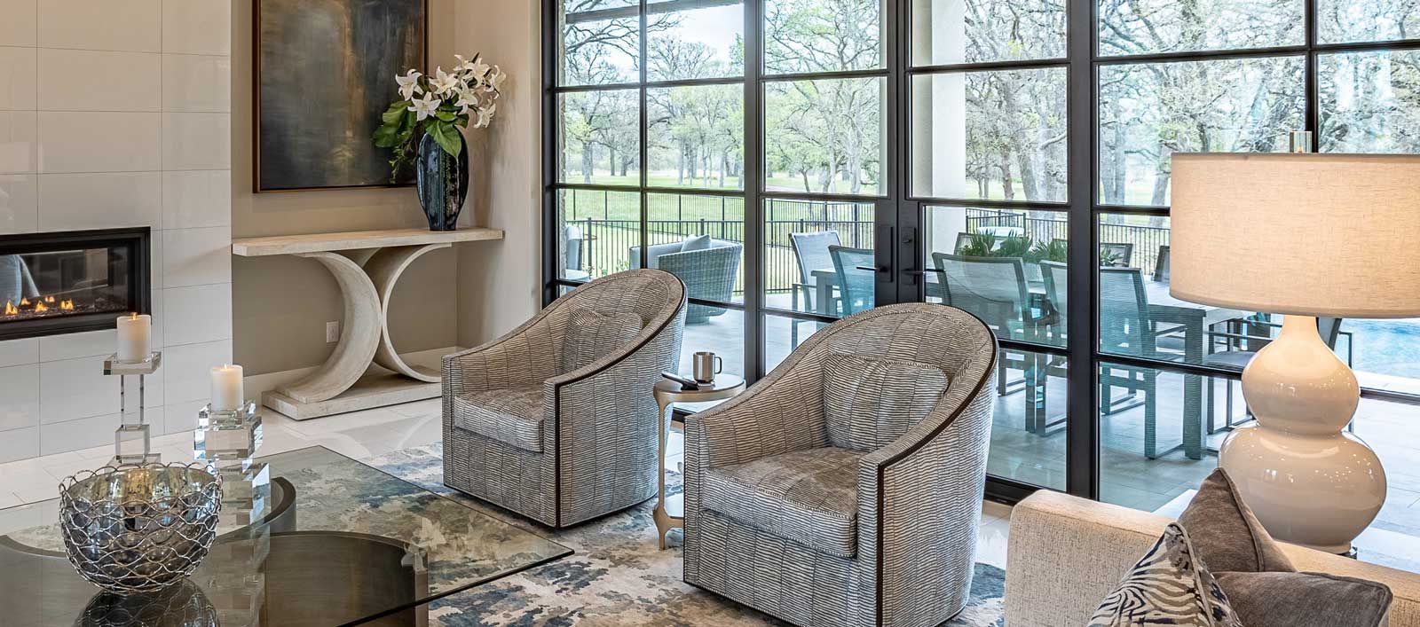 Elegant living room with patterned chairs, fireplace, large windows, and table lamp