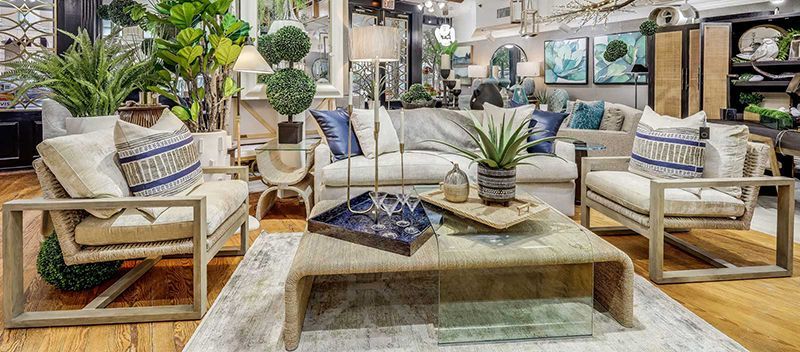 Bright living room with neutral sofas, wooden coffee table, rugs, and many potted plants on shelves and tables