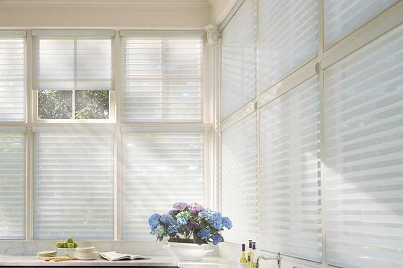 Bright sunlit room with white blinds and a table holding flowers and fruit
