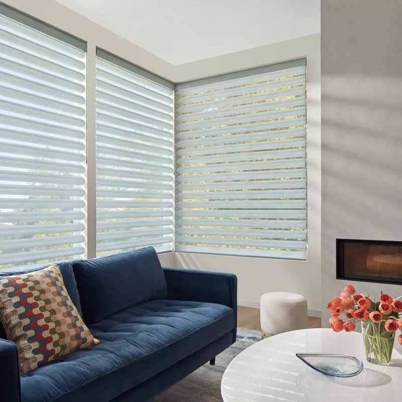 Modern living room with navy sofa, patterned pillow, white coffee table, and large windows with blinds