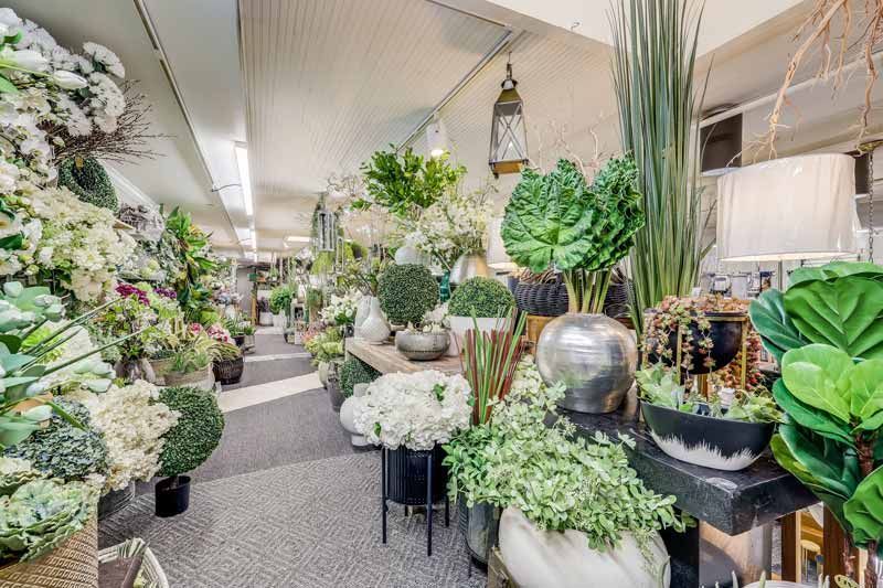 Flower shop aisle filled with white and green floral arrangements and potted plants
