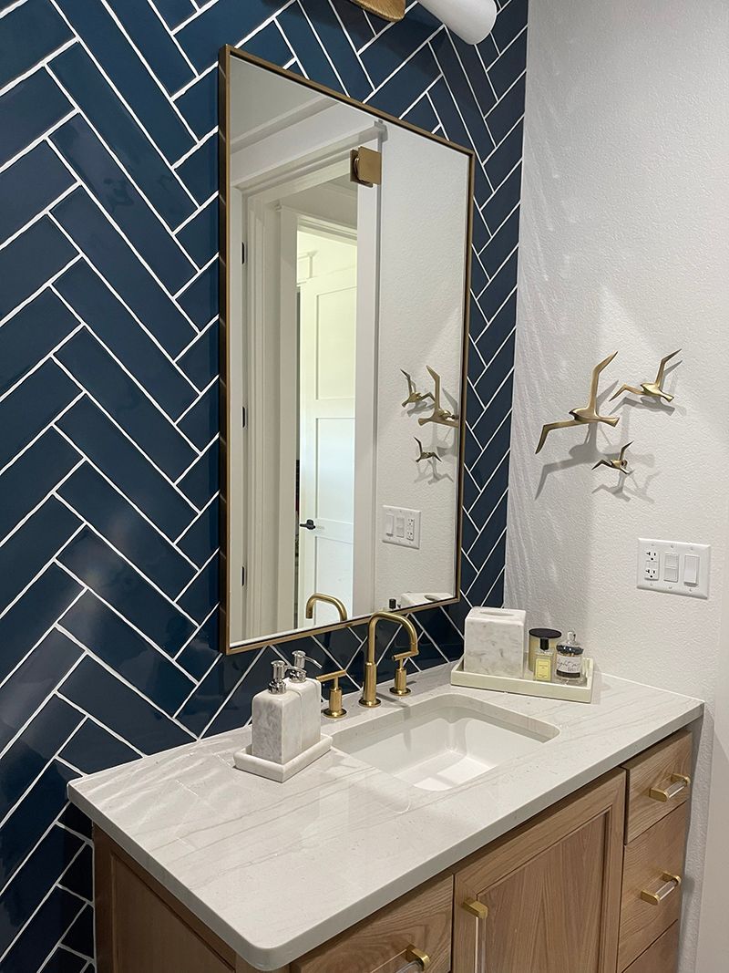 Modern bathroom vanity with white countertop, gold fixtures, navy herringbone tile, and wall mirror