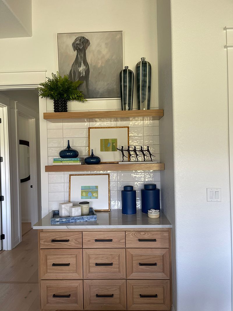 Wooden cabinet with shelves, plants, decor, framed art, and blue canisters in a bright hallway
