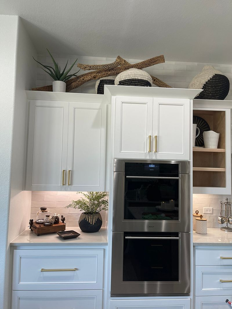 Bright white kitchen with blue lower cabinets, double oven, plants, and decorative countertop accents