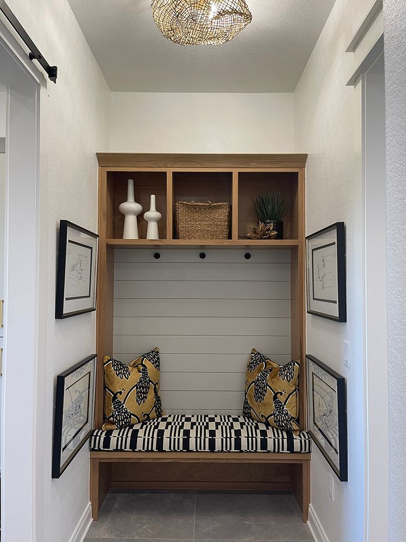Narrow hallway bench nook with striped cushion, patterned pillows, wall shelves, and framed art