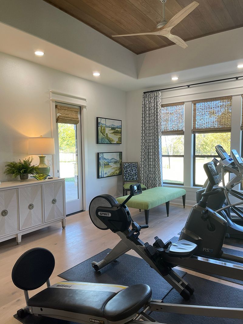 Home gym with exercise bike, weight bench, windows, and neutral decor