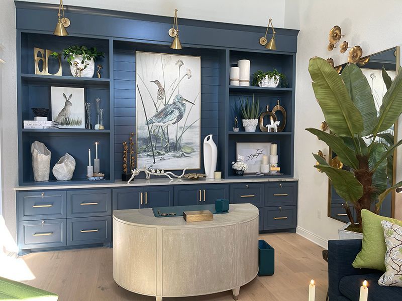 Blue built-in shelving and cabinets with decor around a curved beige table in a bright living room.