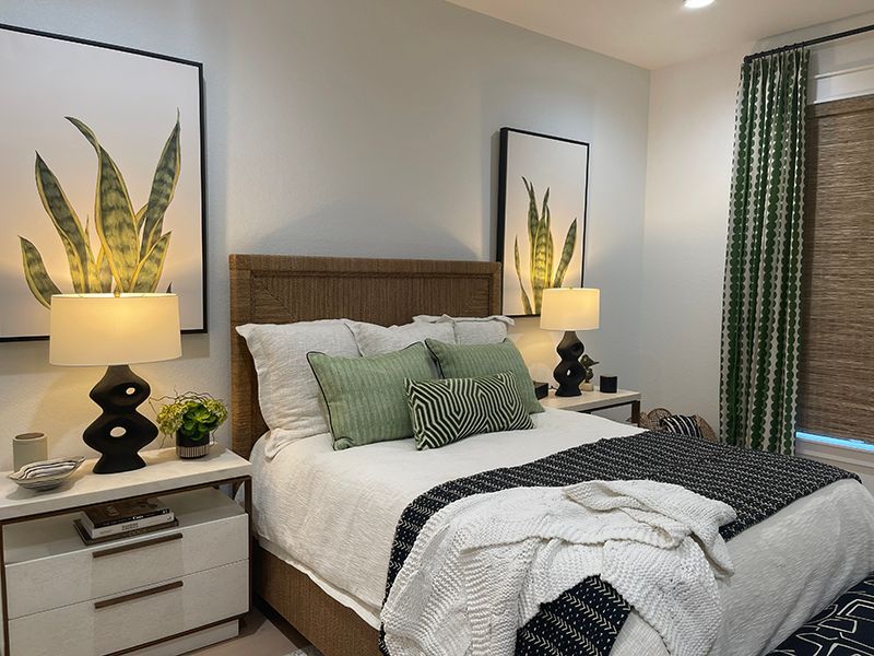 Cozy bedroom with a wooden bed, green accents, bedside lamps, and framed plant prints