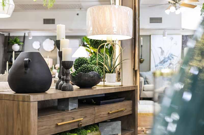 Modern living room with wooden console, black vases, lamp, and lush green plants under a mirror