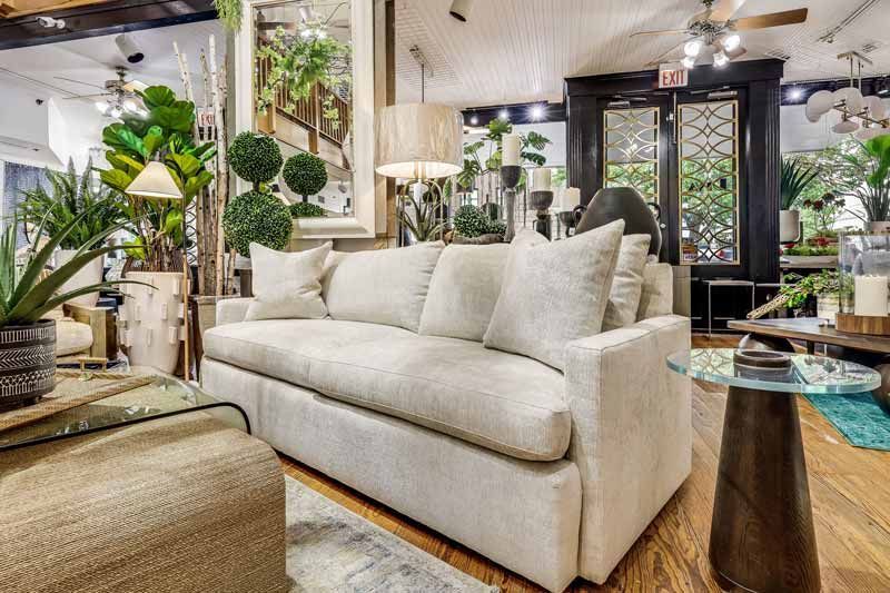 Bright living room with cream sofa, patterned ottoman, plants, and modern decor