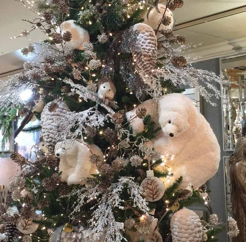 Snowy Christmas tree decorated with white plush bears, pinecones, and frosted ornaments indoors