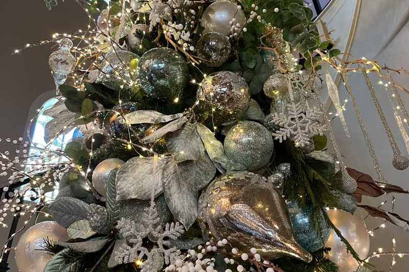 Decorative holiday arrangement with silver and green ornaments, white berries, and glittery branches