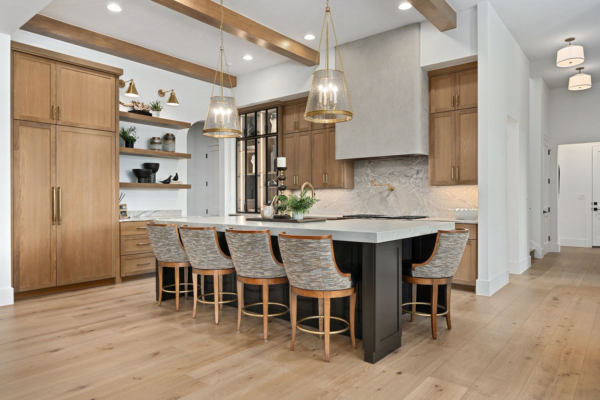 Modern kitchen with wood cabinets, stone island, and upholstered stools on a light wood floor
