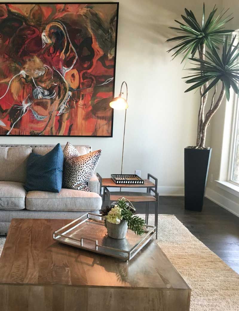 Modern living room with beige sofa, abstract wall art, wooden coffee table, and tall potted plant by a window