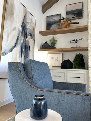 Cozy living room corner with blue armchair, abstract art, shelves, and white cabinet