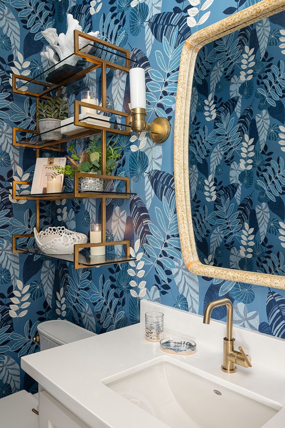 Modern bathroom vanity with gold sink faucet, blue floral wallpaper, and wall-mounted shelves with decor and toiletries
