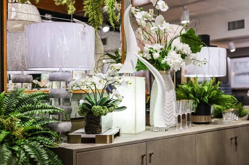 Elegant indoor floral display with white orchids, greenery, and hanging lanterns on a counter