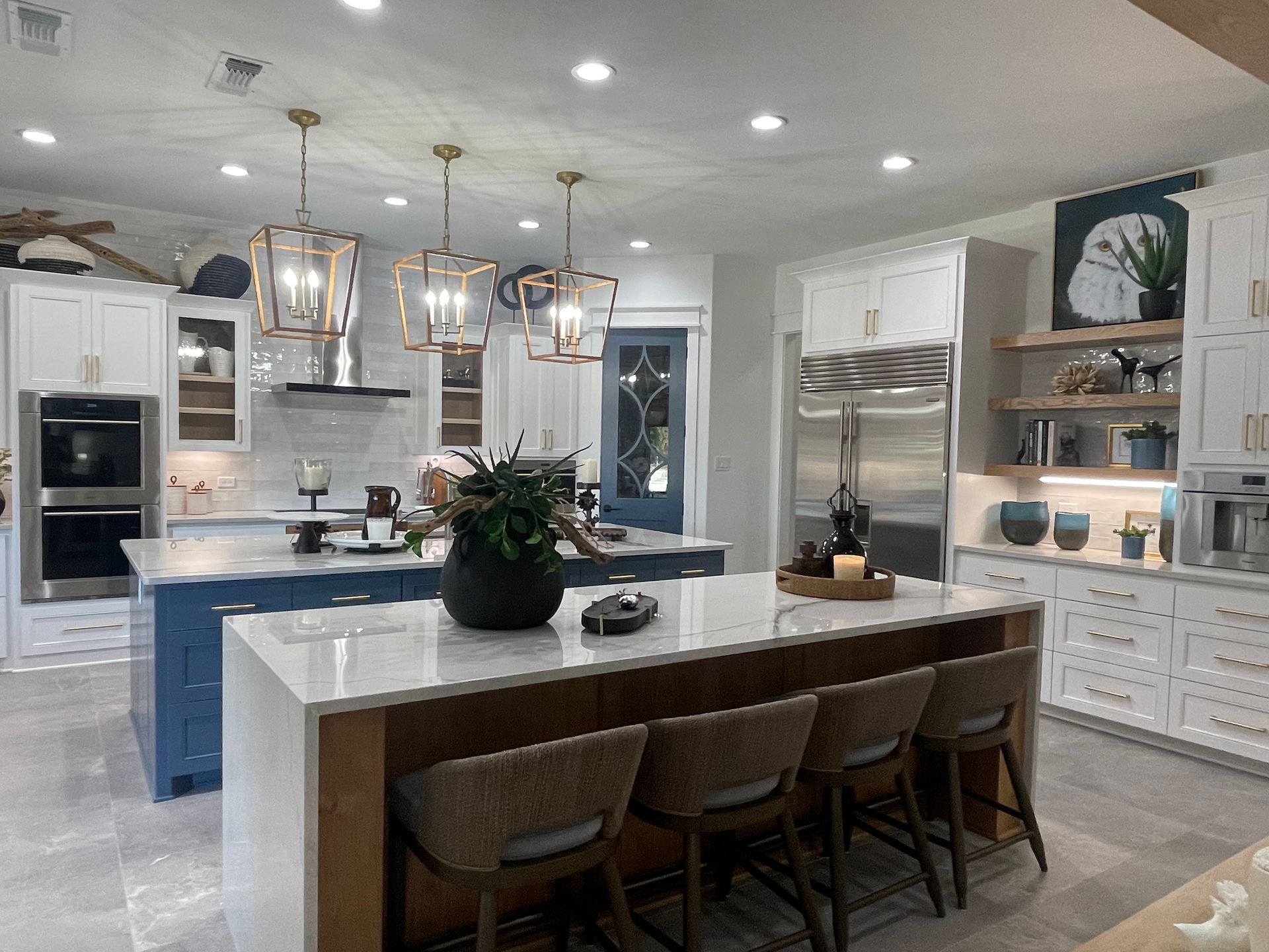 Bright modern kitchen with white cabinets, blue island, marble counters, and pendant lights