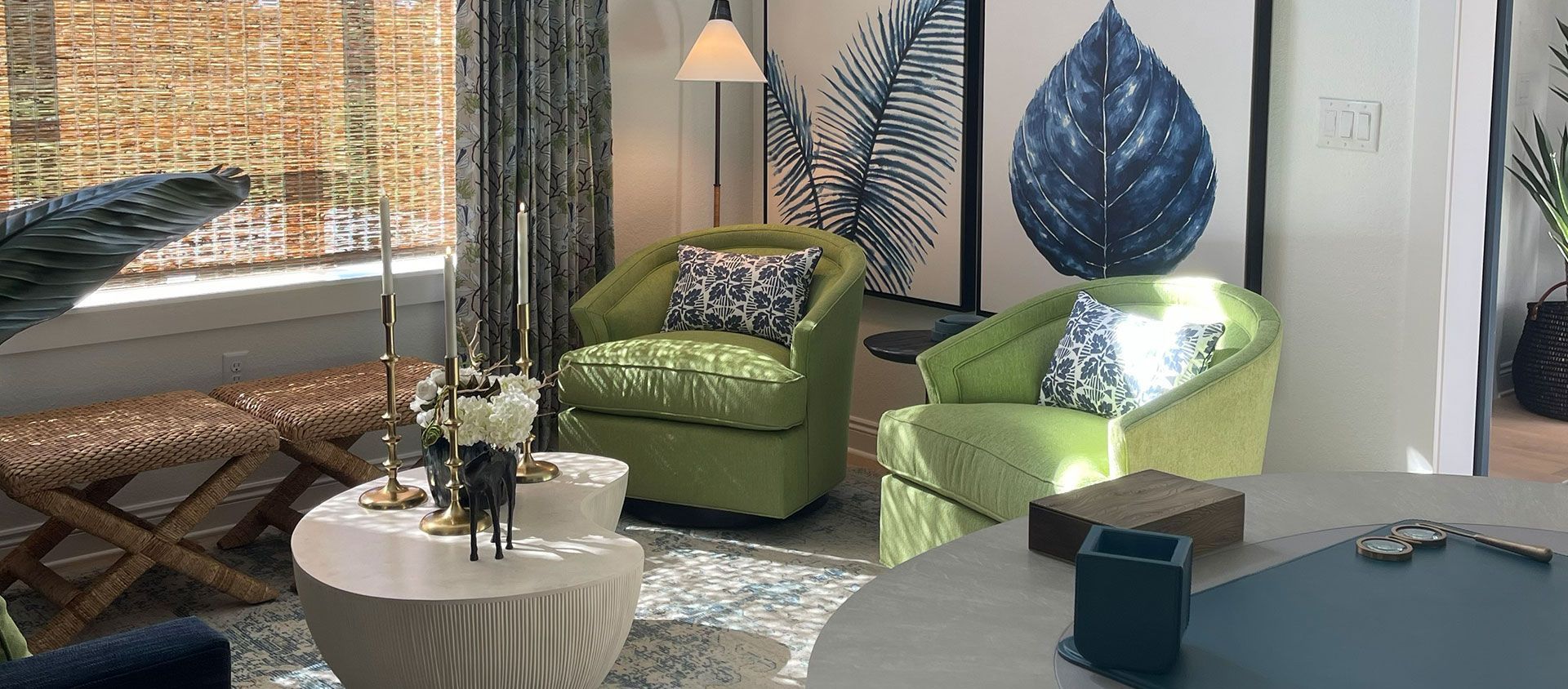Bright living room with green chairs, a white coffee table, patterned rug, and large leaf wall art.