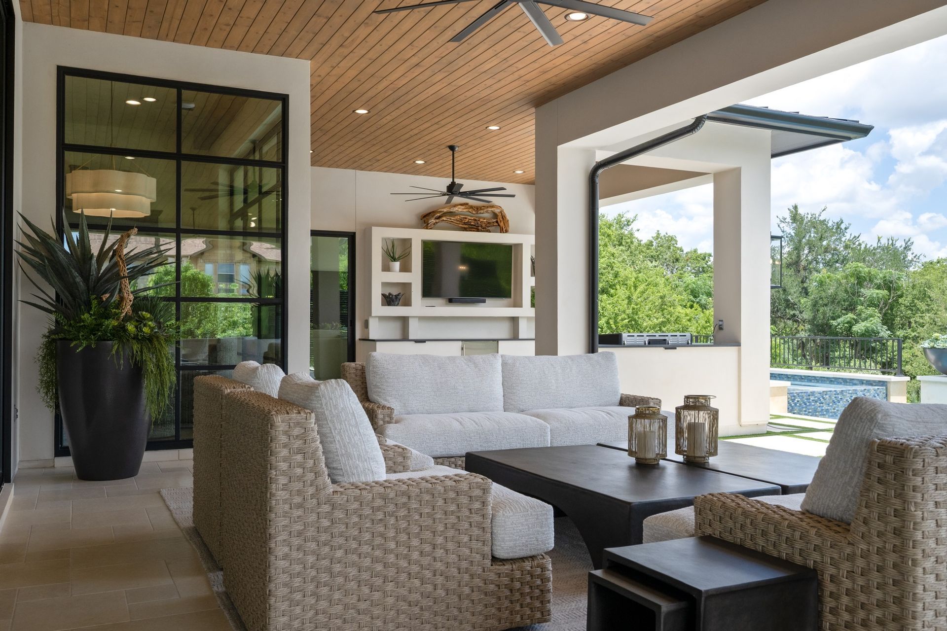 Modern covered patio with wicker seating, dark coffee table, ceiling fans, and a poolside view