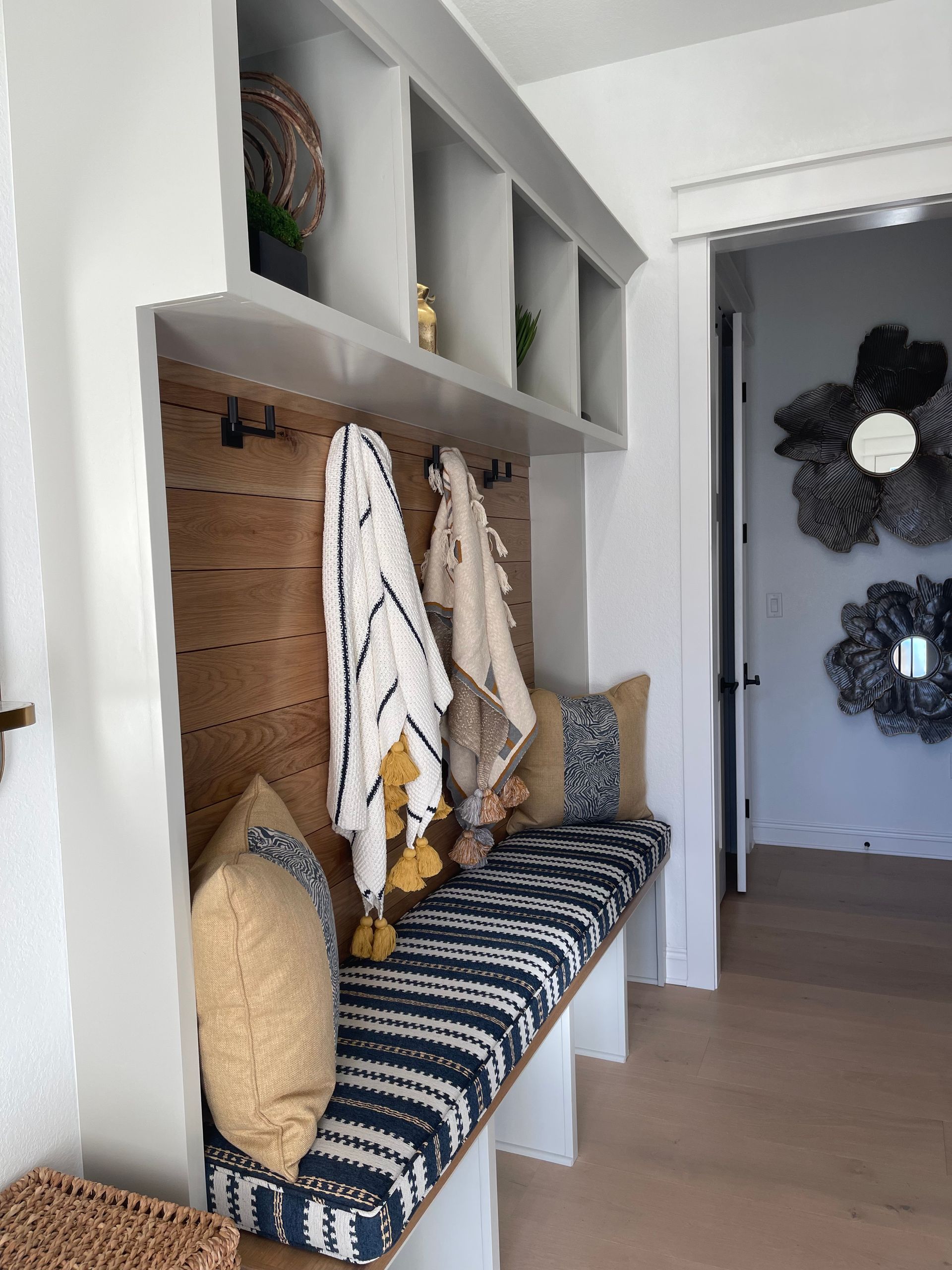 Built-in bench nook with striped cushion, pillows, towels, and wicker baskets in a bright entryway