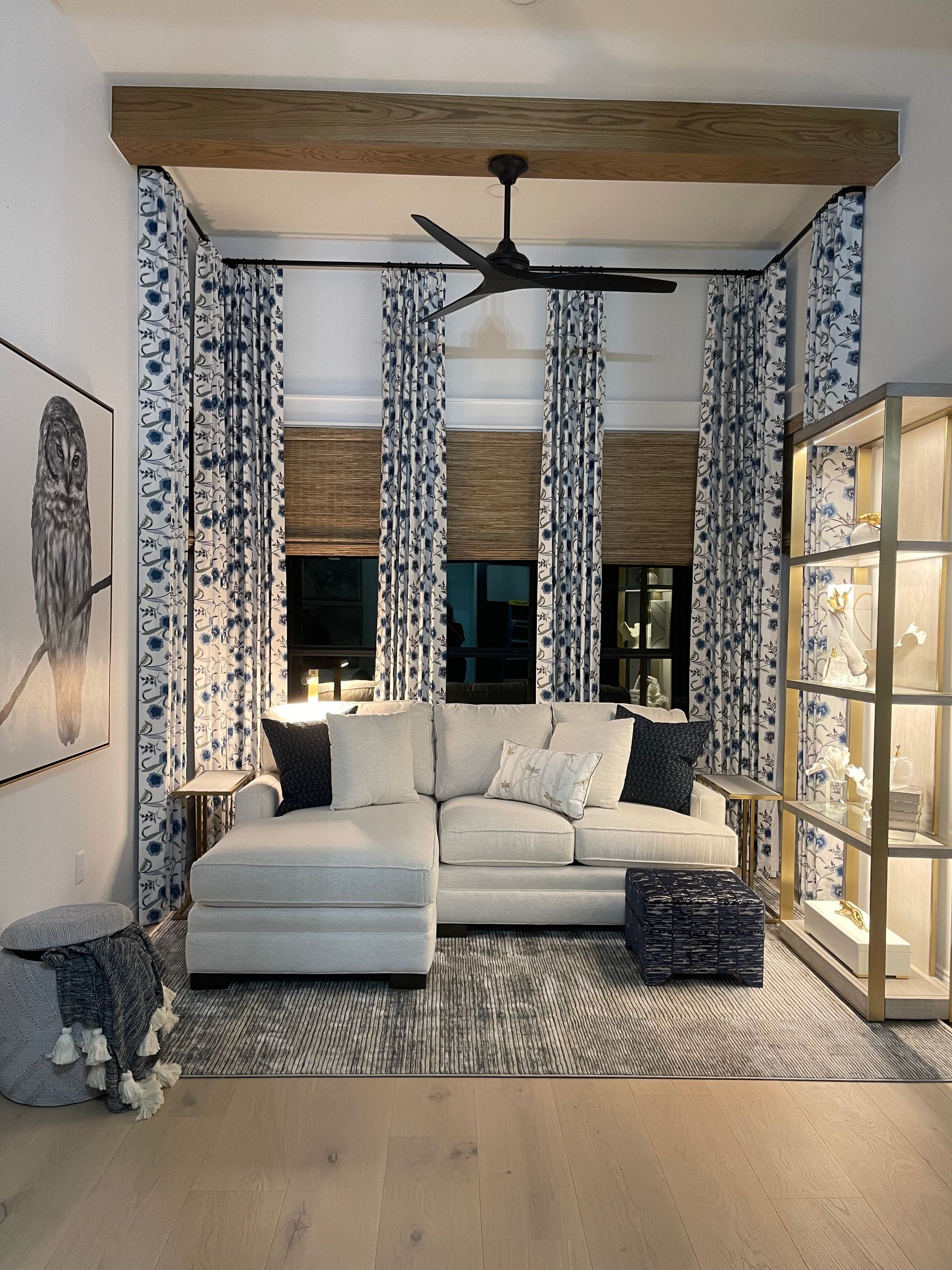 Cozy living room with a white sectional, patterned curtains, ceiling fan, and warm accent lighting.