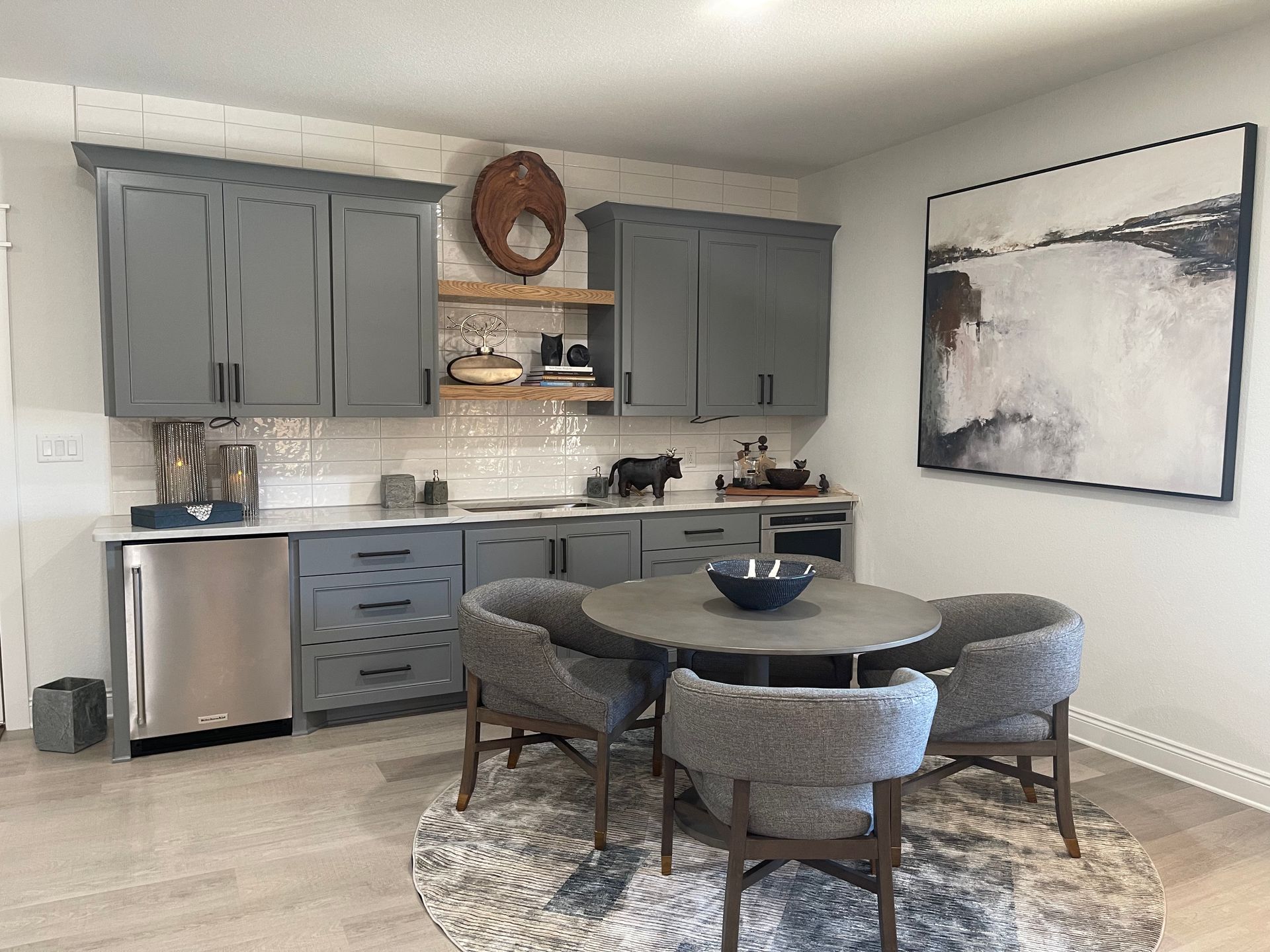 Modern kitchen with gray cabinets, stainless dishwasher, round dining table, and abstract wall art