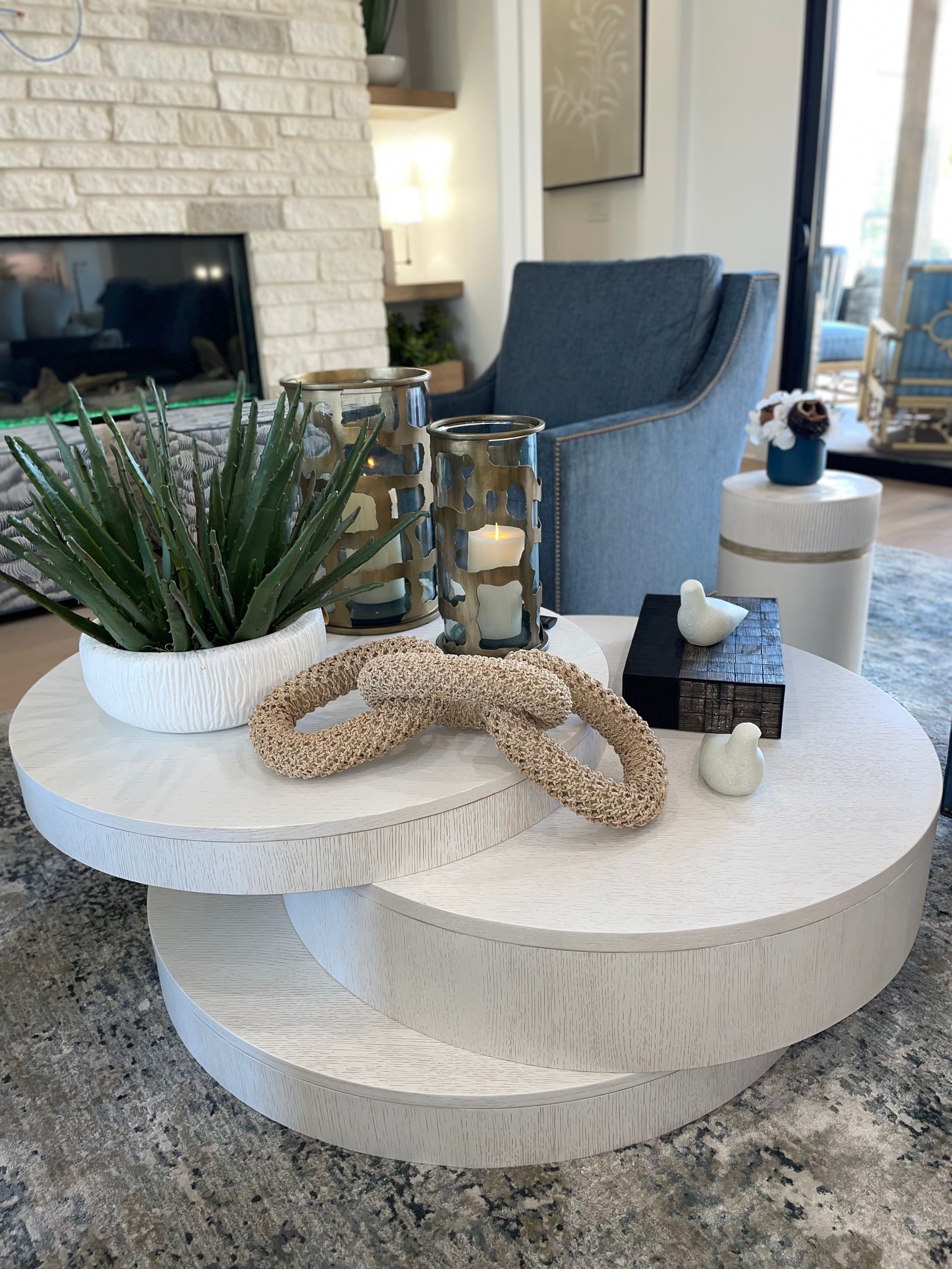 Layered white decorative trays with plant, woven decor, candle, and bottle on a stone coffee table in a living room