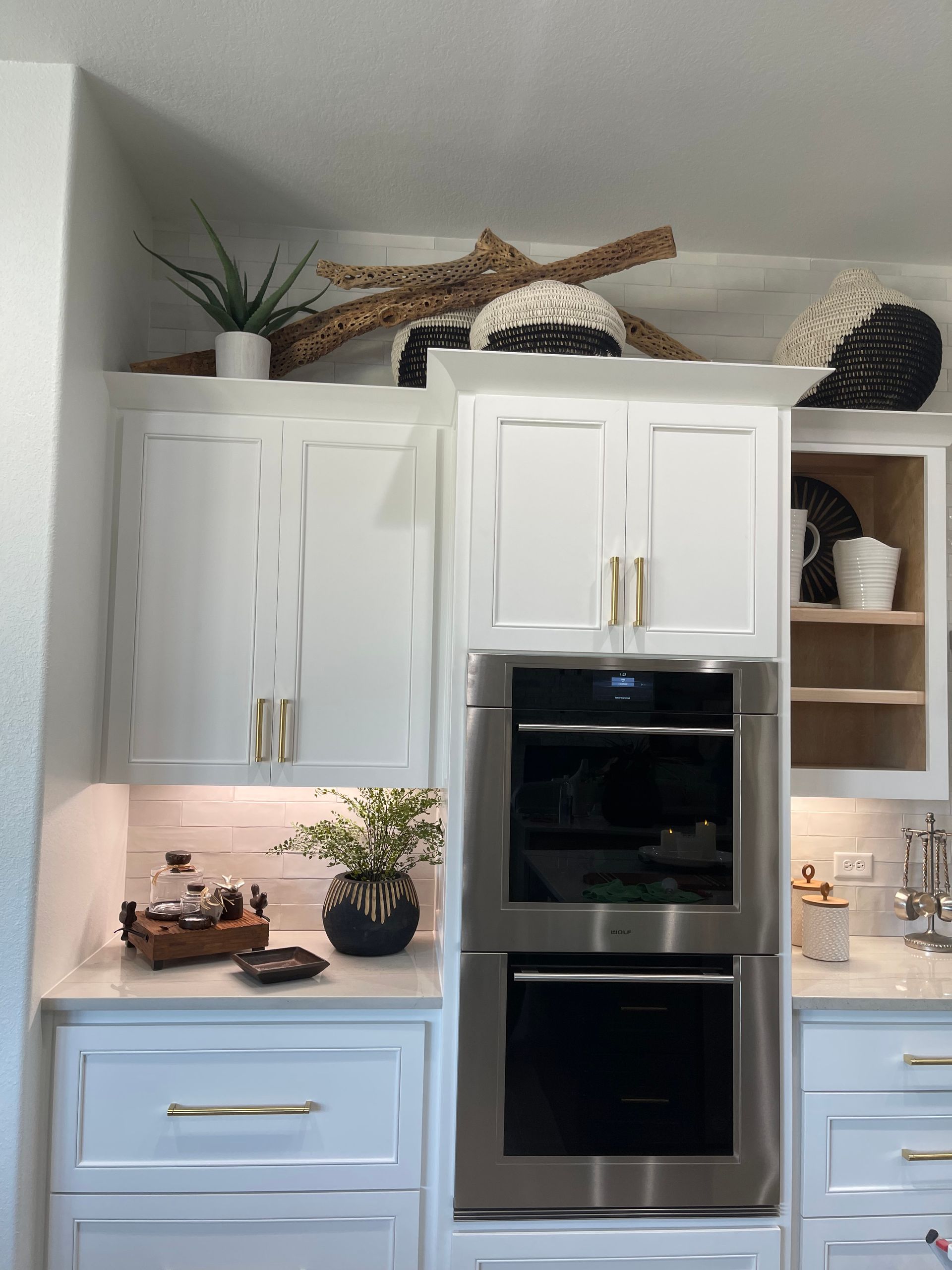 White kitchen with a built-in stainless oven, blue lower cabinets, and open shelves with decor.