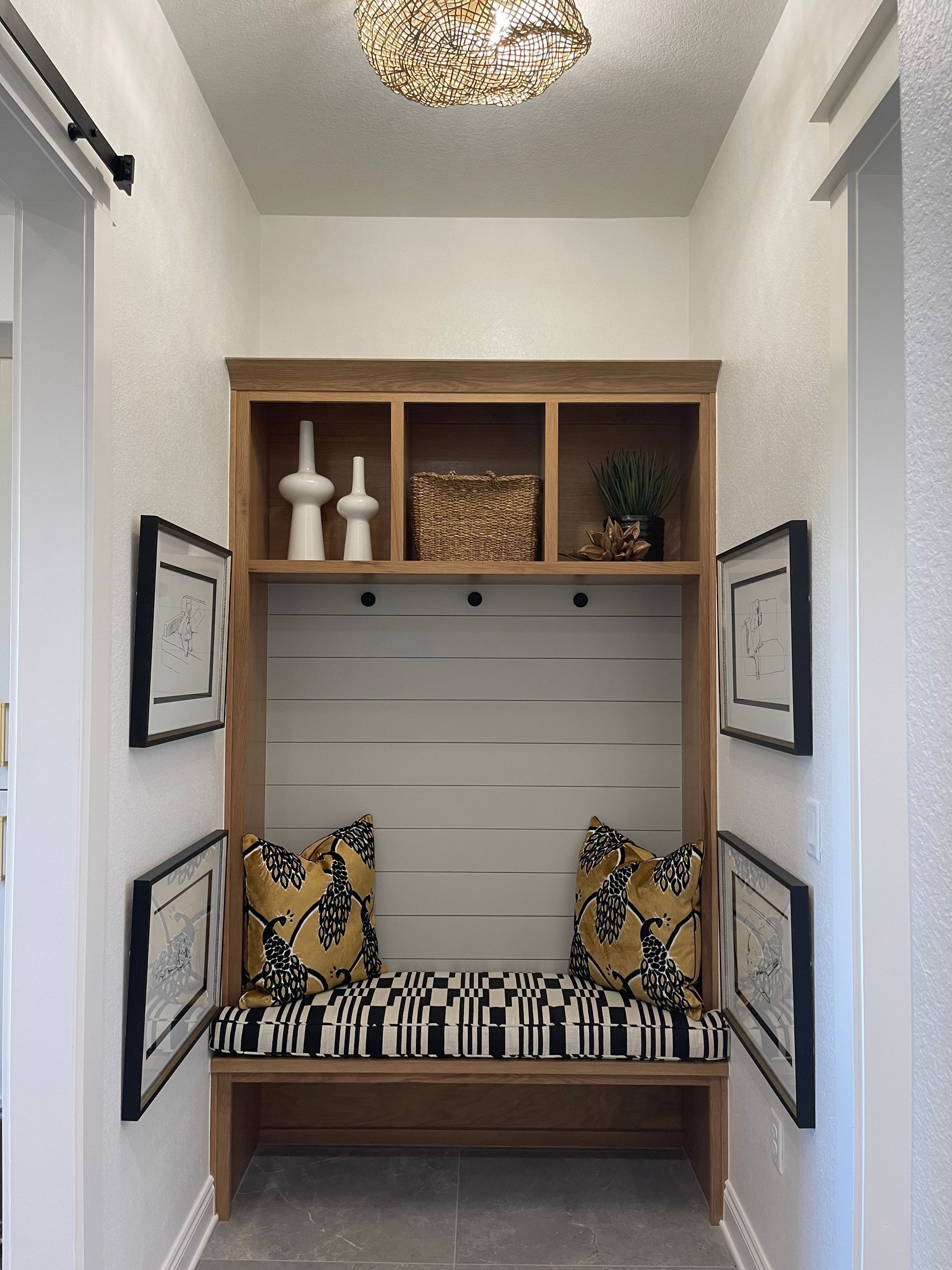 Narrow hallway nook with a striped bench, patterned pillows, wood shelves, and wall art