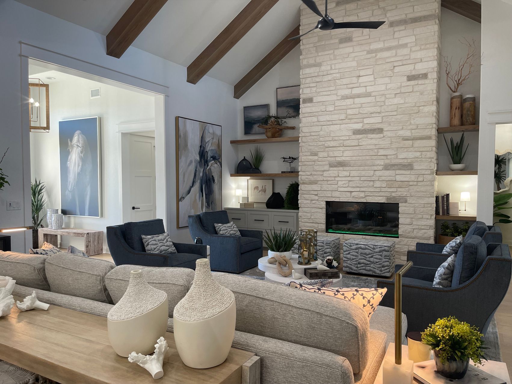 Bright living room with vaulted ceiling, stone fireplace, gray sofas, and blue accents