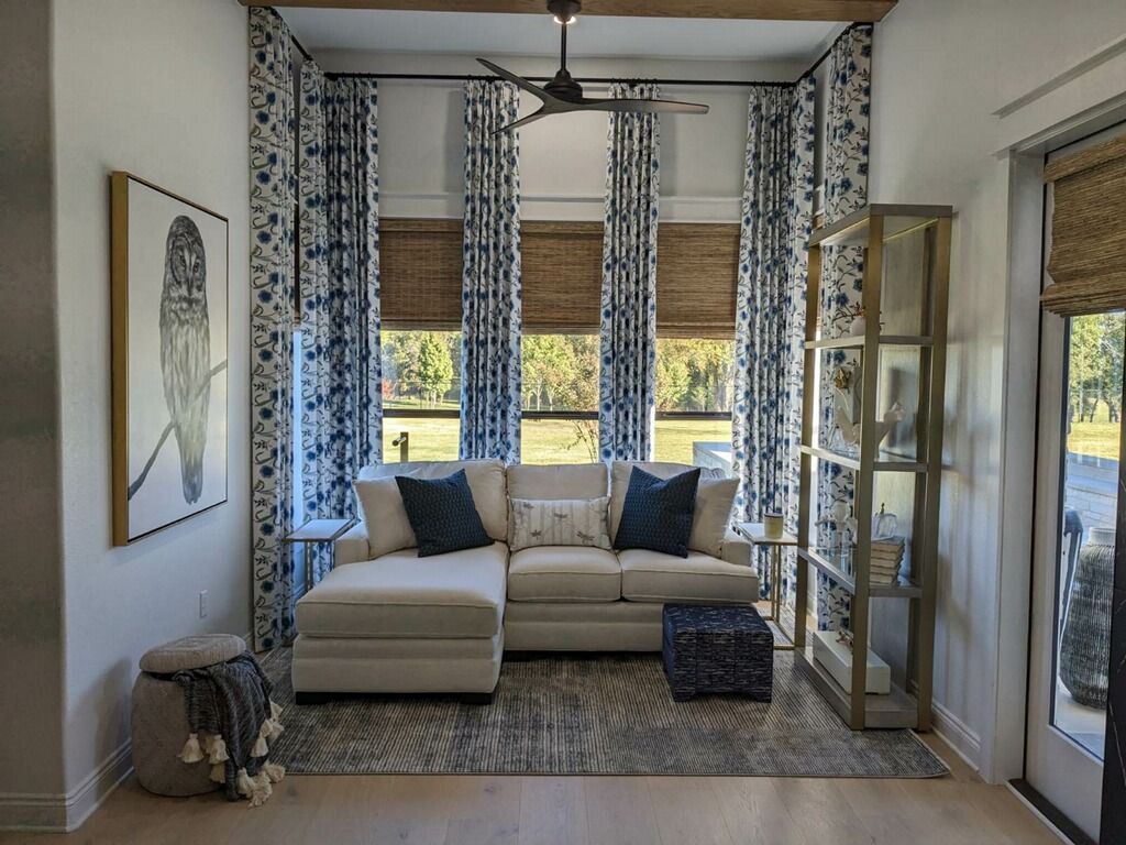 Bright living room with white sectional sofa, patterned curtains, large windows, and a glass door to the patio