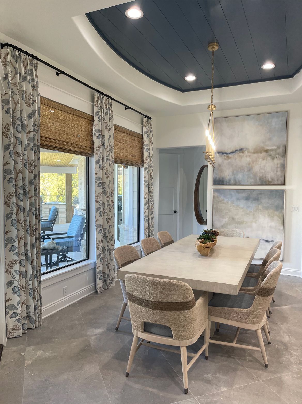 Modern dining room with a wood table, woven chairs, large windows, and a dark blue tray ceiling